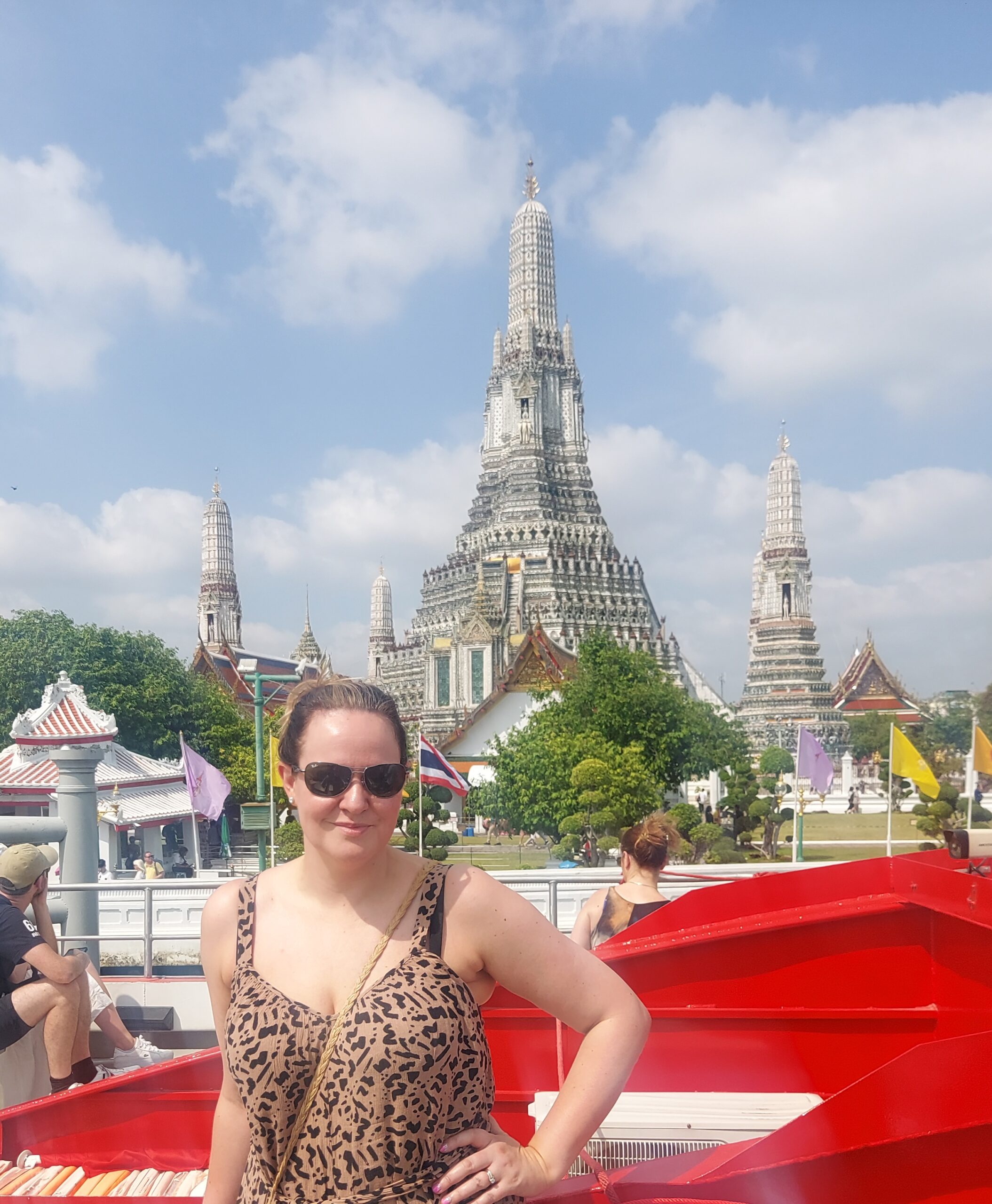 Leanne in front of Bangkok’s Wat Arun temple on a sunny day, wearing sunglasses with the ornate spires rising behind her.