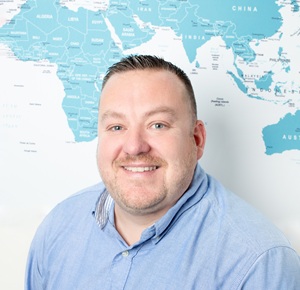 Andy profile photo in the eShores office, standing in front of a large world map.