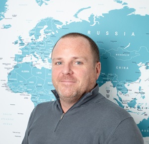 Profile photo of Dave standing in front of the office world map, smiling with a clean, professional backdrop.