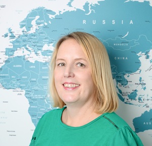 Profile photo of Hannah, smiling warmly in the office with the large world map behind her.