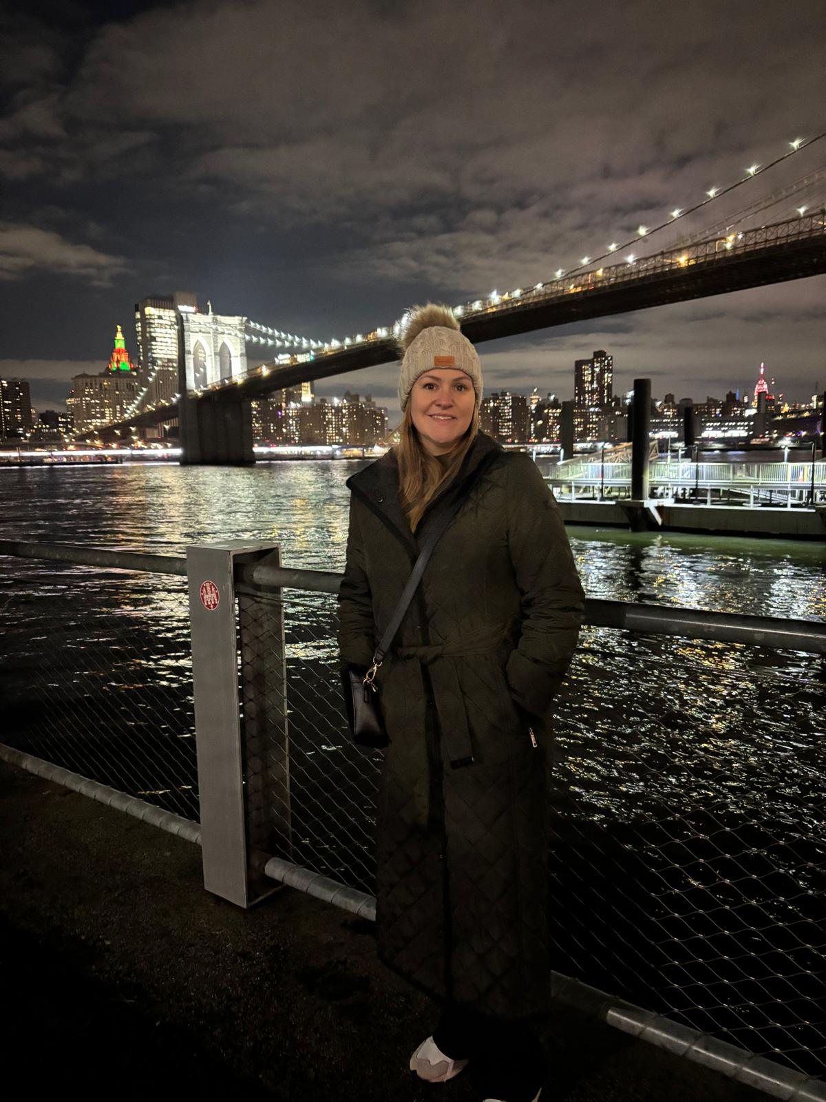 Leanne in New York at night with the city skyline glowing behind her.
