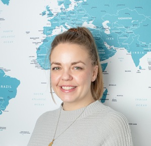 Laura in front of the office map, smiling for a staff profile photo.