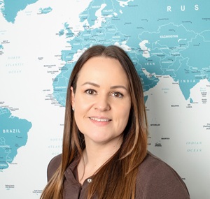 Leanne smiling outdoors, wrapped in a scarf and hat in Lapland, with reindeer behind her against a snowy winter landscape.