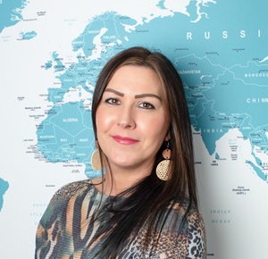 Profile photo of Michelle in the office, standing in front of the large world map.