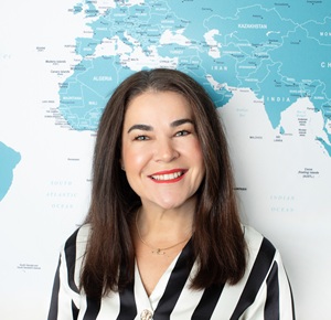 Nadine in the office, smiling while seated at her desk with the wall map behind her.
