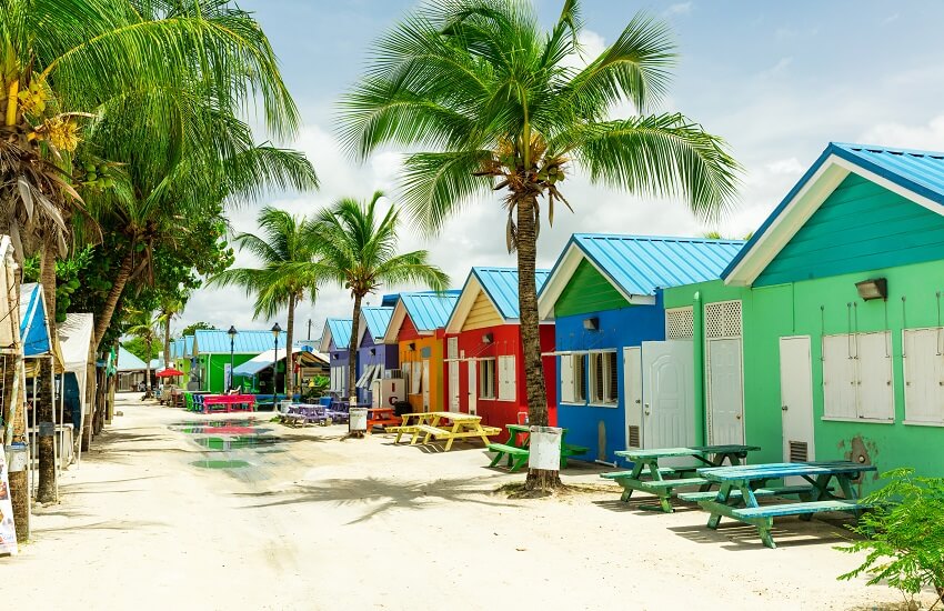 Oistins Fish Market in Barbados during the day, showing colourful huts, picnic benches and scattered palm trees.