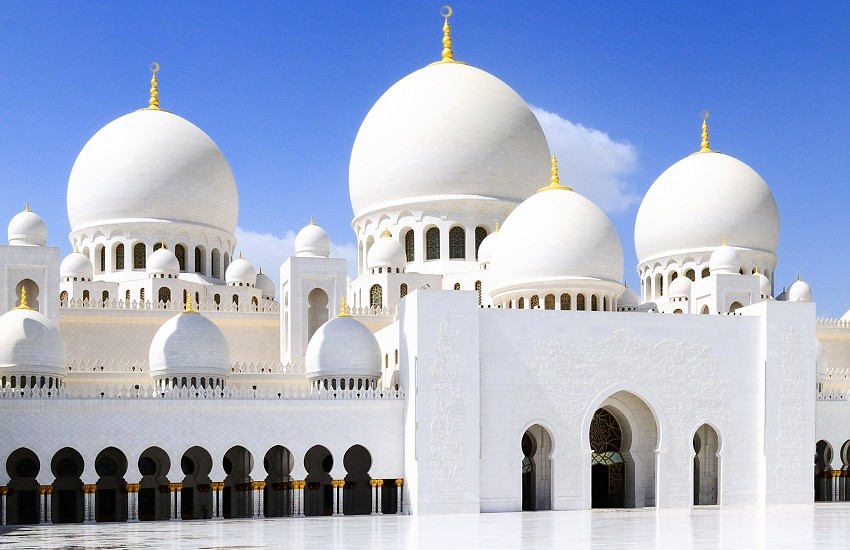 The White Mosque of Abu Dhabi gleaming under a bright blue sky, with its domes and arches standing in crisp contrast.