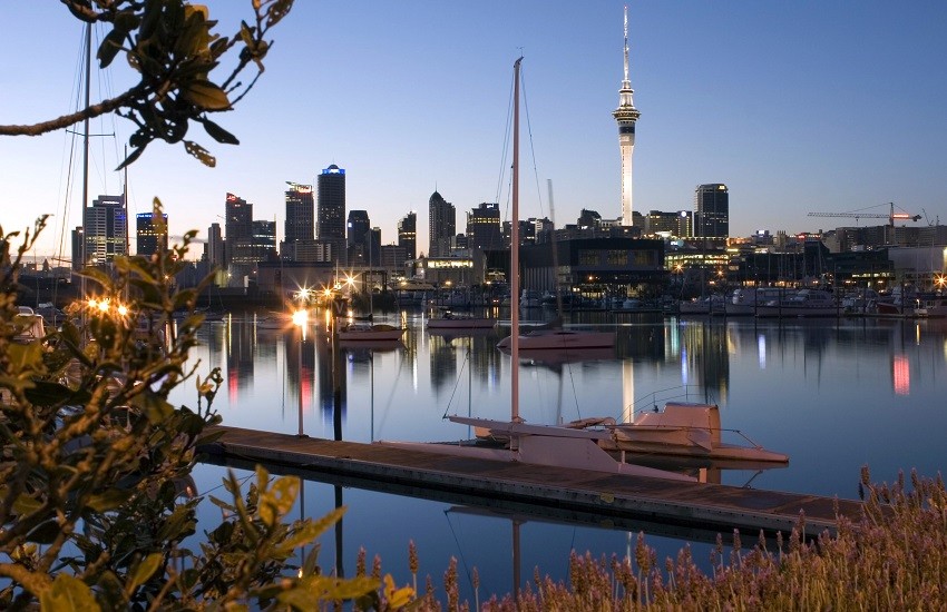 Auckland Harbour at dusk with city lights reflecting on the water under a blue sky