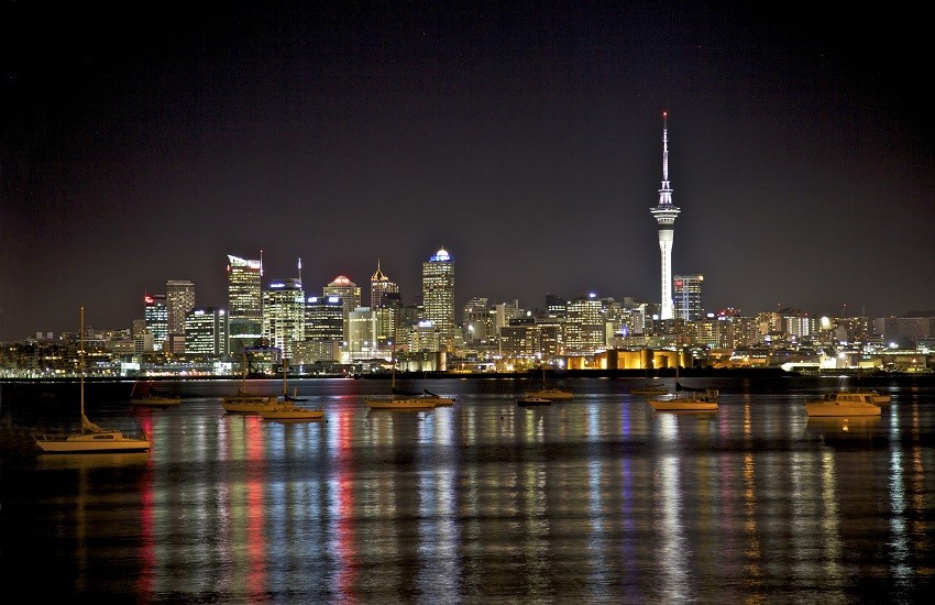 Auckland city skyline at night on New Zealand’s North Island, with lights reflecting on the water