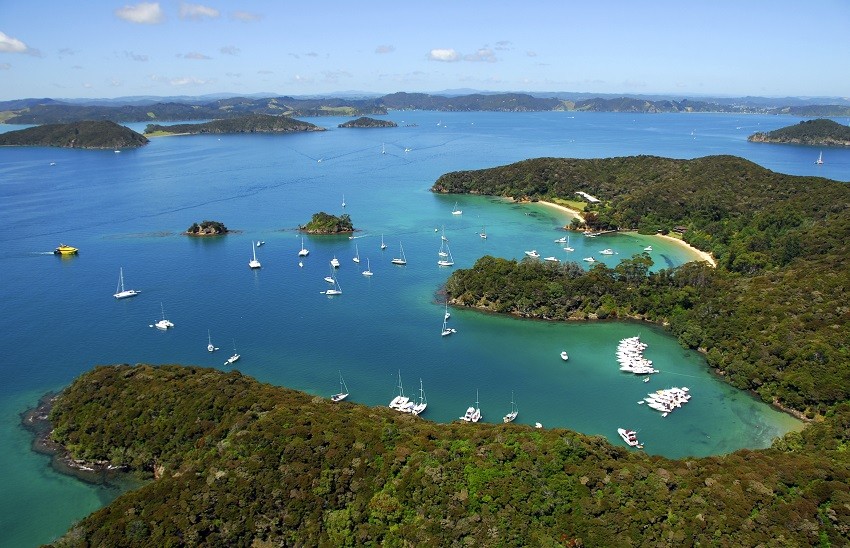 Aerial view of the Bay of Islands in New Zealand with yachts moored in sheltered bays, surrounded by lush green islands and vivid blue waters