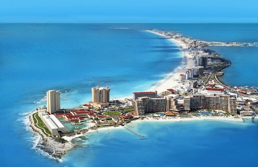 Aerial shot of Cancun’s hotel zone with vivid blue ocean, white-sand beaches and the coastline curving around the resorts.