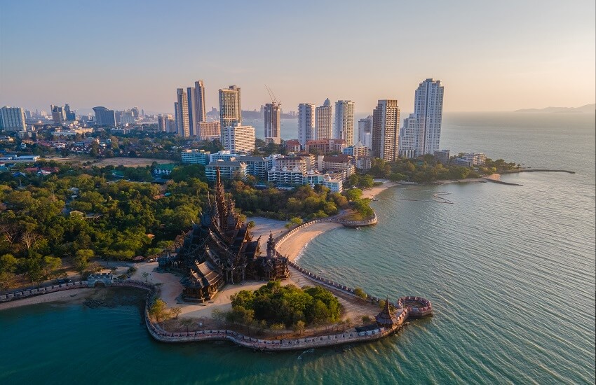 A coastal temple in Pattaya with modern skyscrapers behind it and gentle seas lapping against the shoreline.