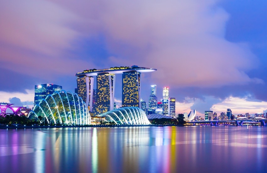 Singapore skyline at twilight, with futuristic skyscrapers glowing purple around Marina Bay and the Singapore Flyer to the right.