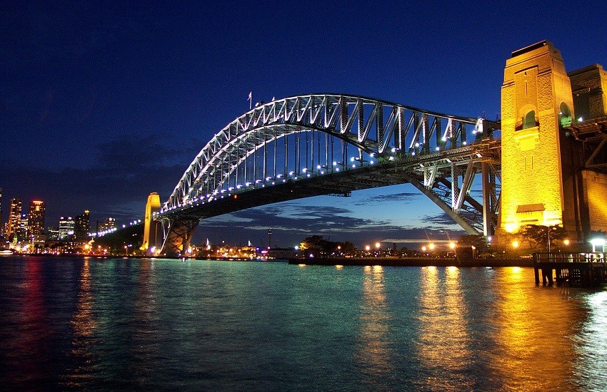 Sydney Harbour Bridge illuminated at night with the city lights reflecting on the water.
