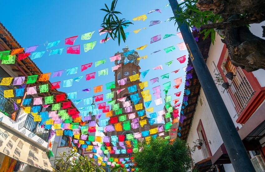 A Puerto Vallarta street with colourful bunting strung overhead and a church visible in the background.
