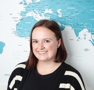 Profile picture of Amy standing in front of the office world map.