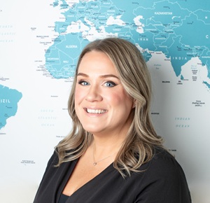 Claire standing in front of the office map, smiling, in a bright indoor setting.