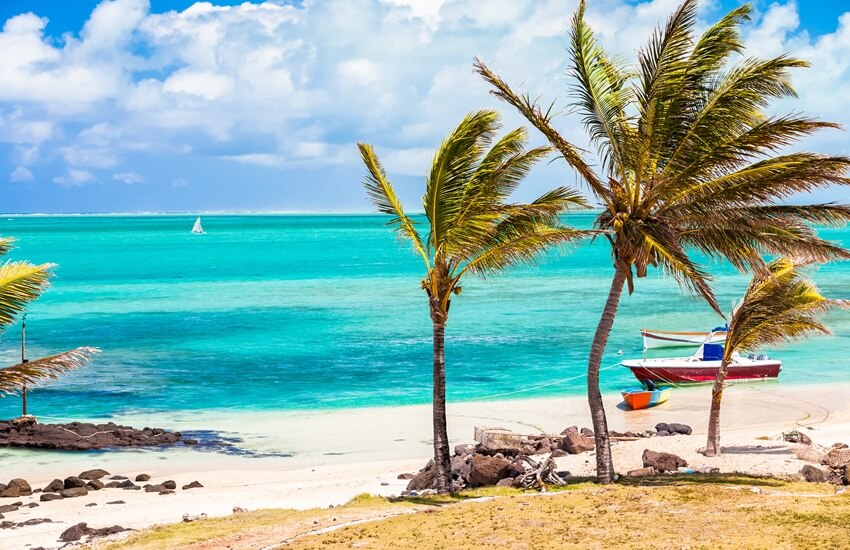 Deserted Plage Mourouk beach in Rodrigues with palm trees blowing in the wind, turquoise waters and small boats resting on the sand